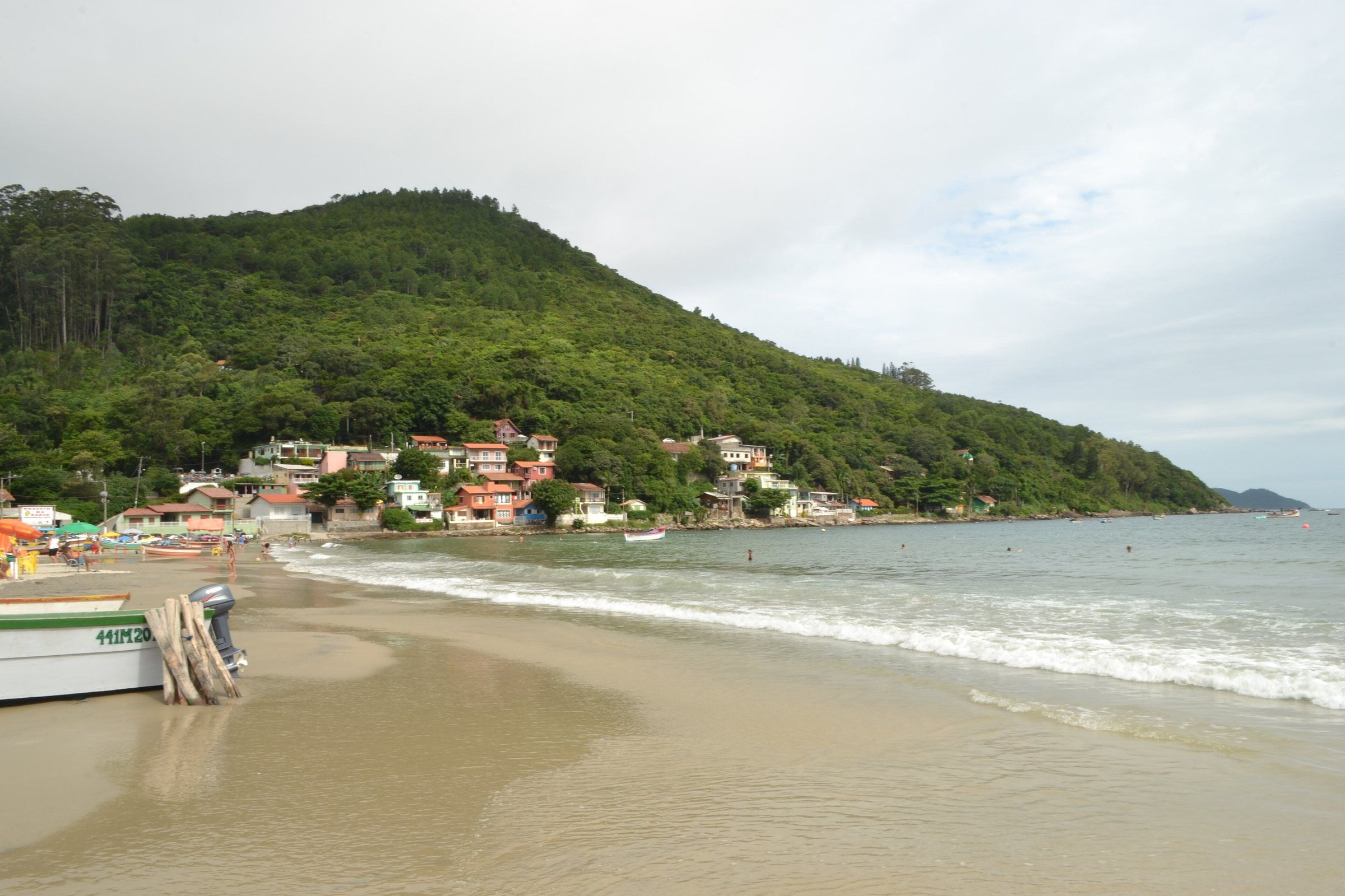 A praia do Pântano do Sul com um barco de pesca na areia e o morro verde ao fundo