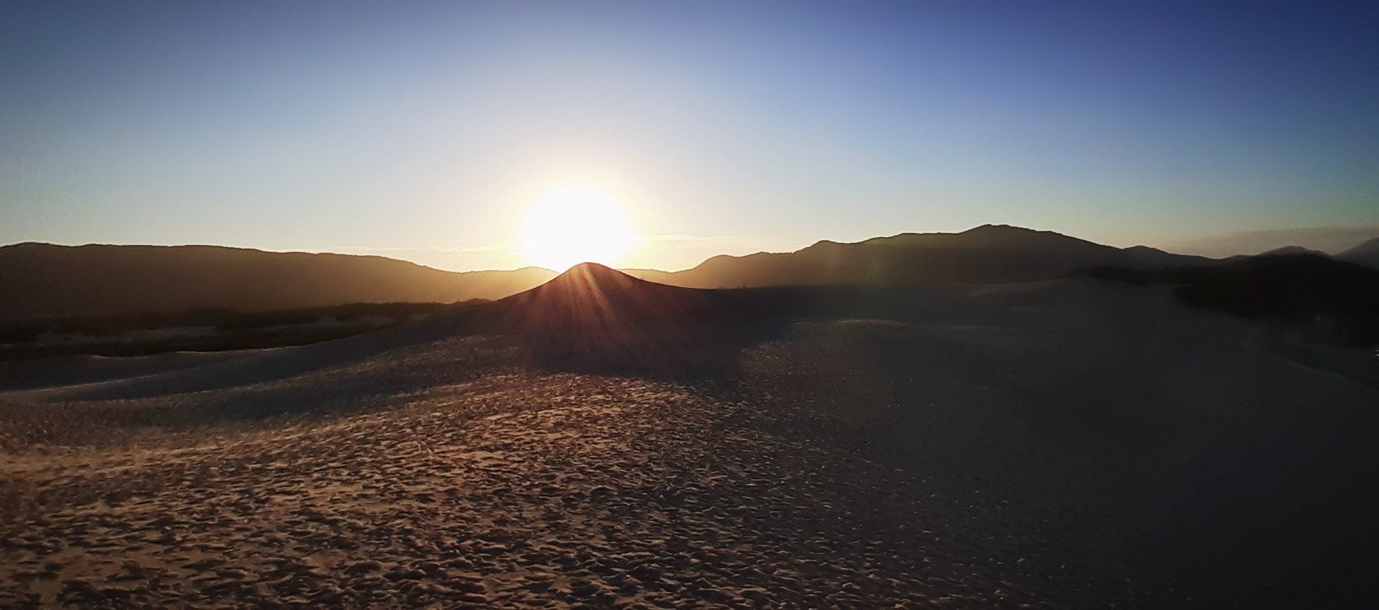 O sol se pondo atrás dos morros, visto do alto das dunas da Joaquina