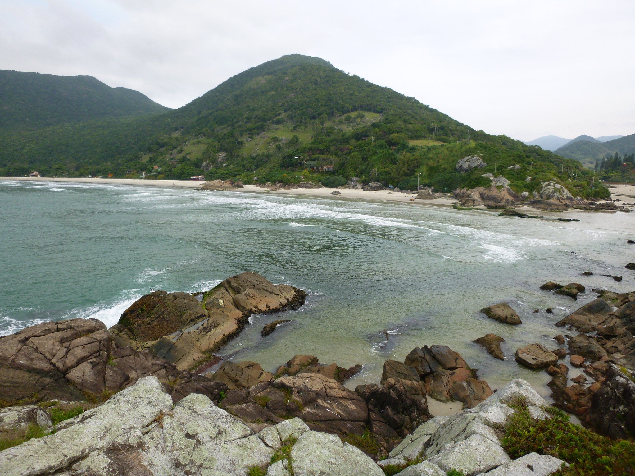 A Praia do Matadeiro com pedras em primeiro plano, a areia e o morro verde ao fundo